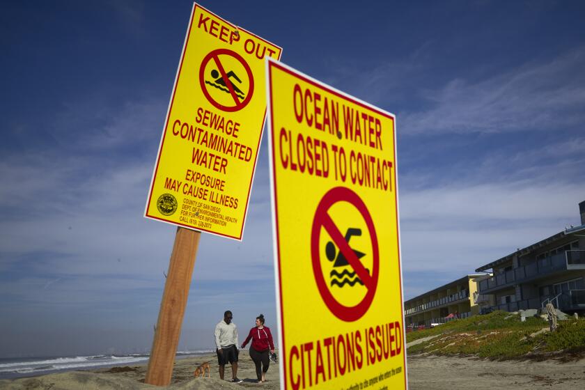 FILE - In this Dec. 12, 2018, file photo, a couple walk along the beach as signs warn of contaminated water at Imperial Beach, Calif. The entire shoreline of Southern California's Imperial Beach is closed to swimmers and surfers after sewage-contaminated runoff flowed north again from Mexico’s Tijuana River. The closure announced Friday, April 16, 2021, will be in place until testing shows the water is safe, the San Diego Union-Tribune reported. (AP Photo/Gregory Bull, File)
