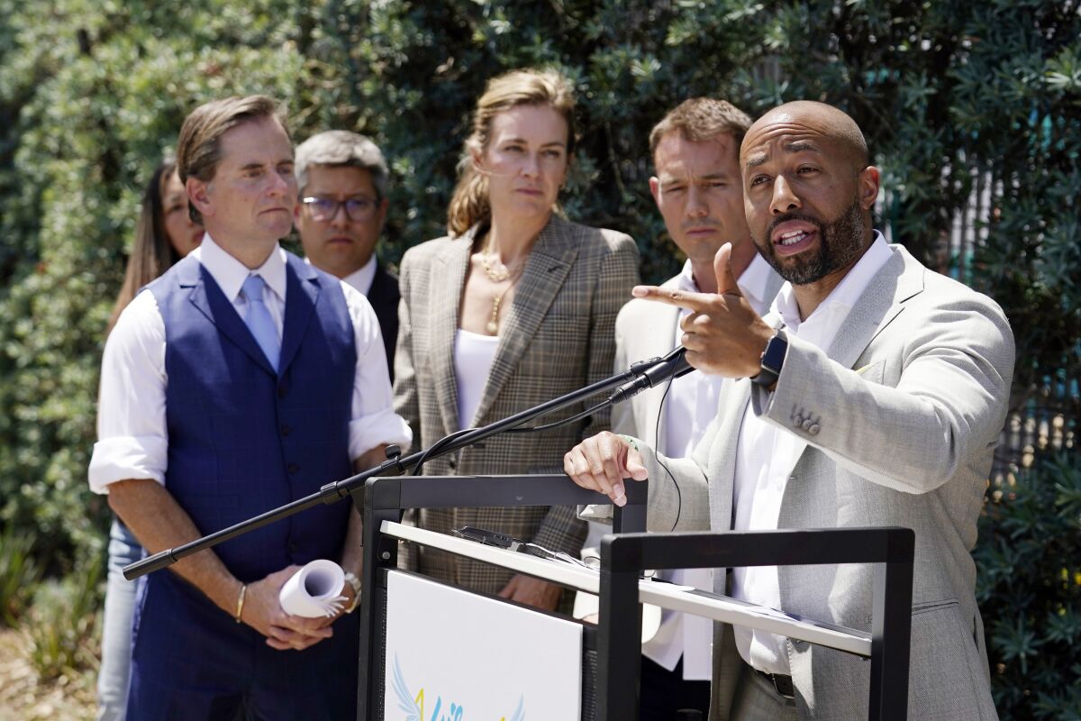 Charles Johnson, right, is surrounded by his legal team Chris Dolan, left, in blue, Courtney Rowley, center, and Nick Rowley, second from right, during a press conference announcing a lawsuit outside Cedars-Sinai Medical Center, Wednesday, May 4, 2022, in Los Angeles. Johnson's wife Kira died at the hospital in 2016 from complications after giving birth by cesarean section. (AP Photo/Marcio Jose Sanchez)