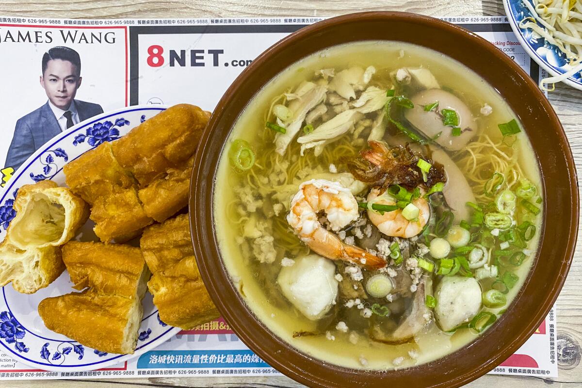 A bowl of soup with vegetables and shrimp, with a side of you tiao