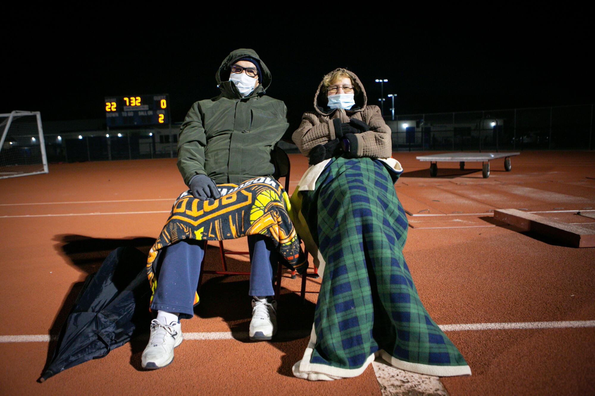 Raymond and Caroline Burt watch the game while bundled up in coats and blankets.
