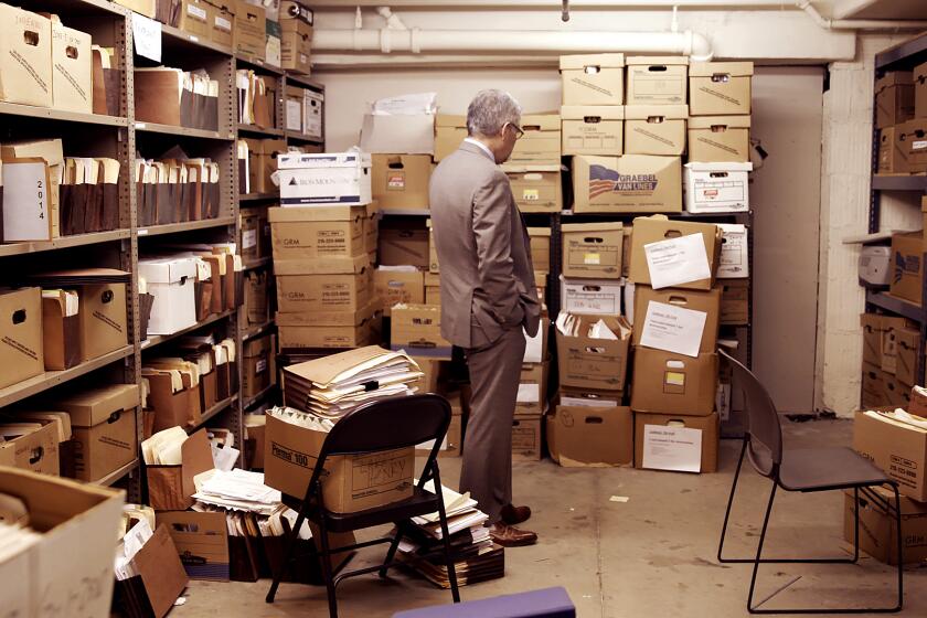 A man in a gray suit stands in a room lined with boxes