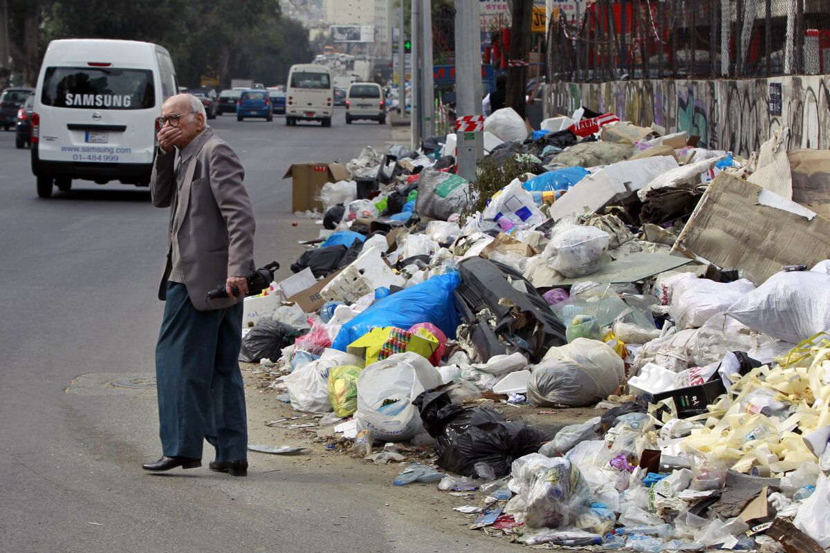 A man covers his nose from the smell as he walks past a pile of garbage on a street in Beirut.