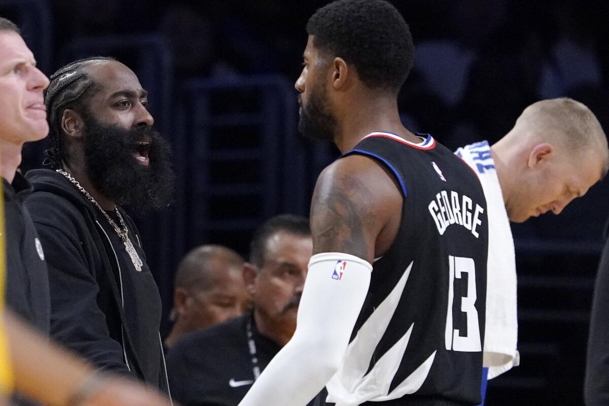 Clippers guard James Harden celebrates during a timeout as forward Paul George walks back to the bench.