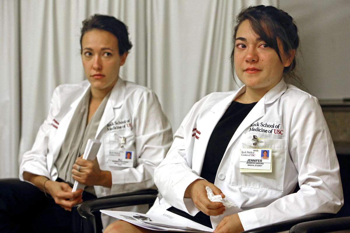 Ali Shannon Philander, left, and Jennifer Sakioka, medical students in the Keck School of Medicine of USC in Boyle Heights, show their emotions after treating David Solomon, a hospice patient portrayed by actor Bob Rumnock.