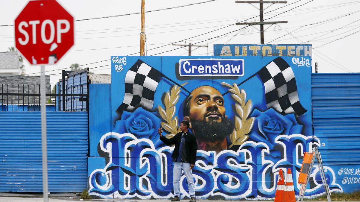 A passerby takes a selfie with a mural of Nipsey Hussle on the 3400 block of Slauson Avenue in South Los Angeles. (Luis Sinco / Los Angeles Times)