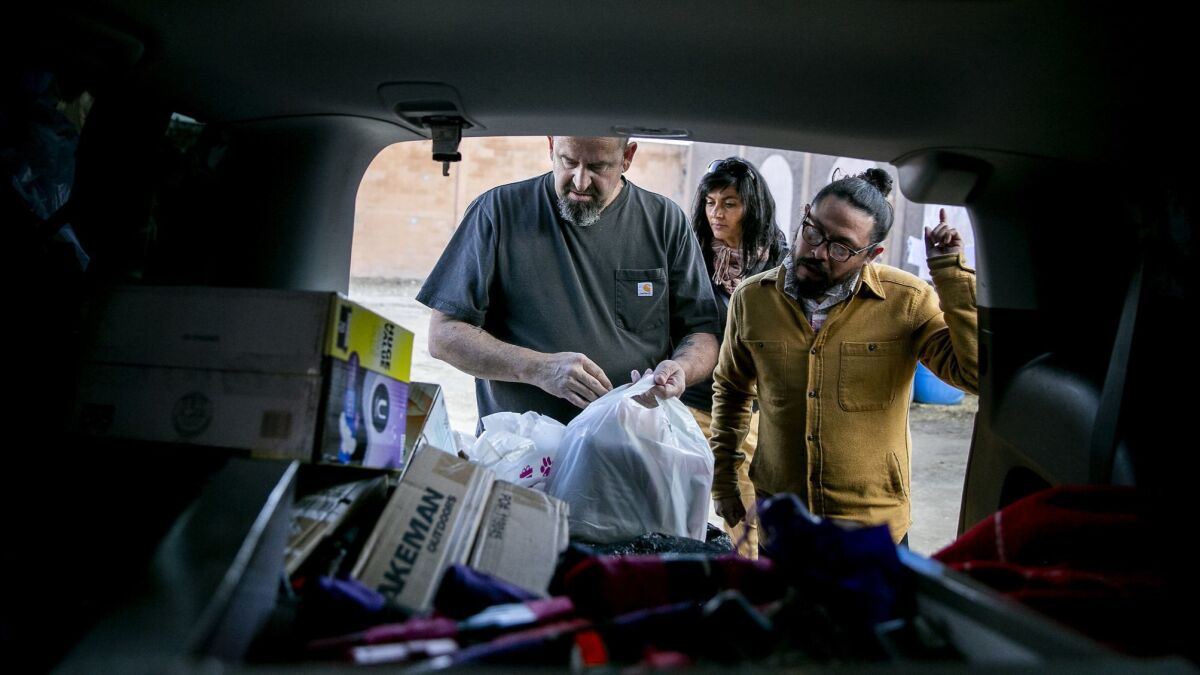 Mark Lane, left, of the Minority Humanitarian Foundation hands out supplies at a migrant shelter in the Matamoros neighborhood in Tijuana.