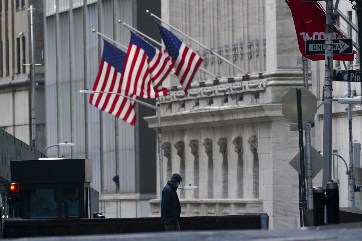 A person walks near a building with three U.S. flags flying in front.