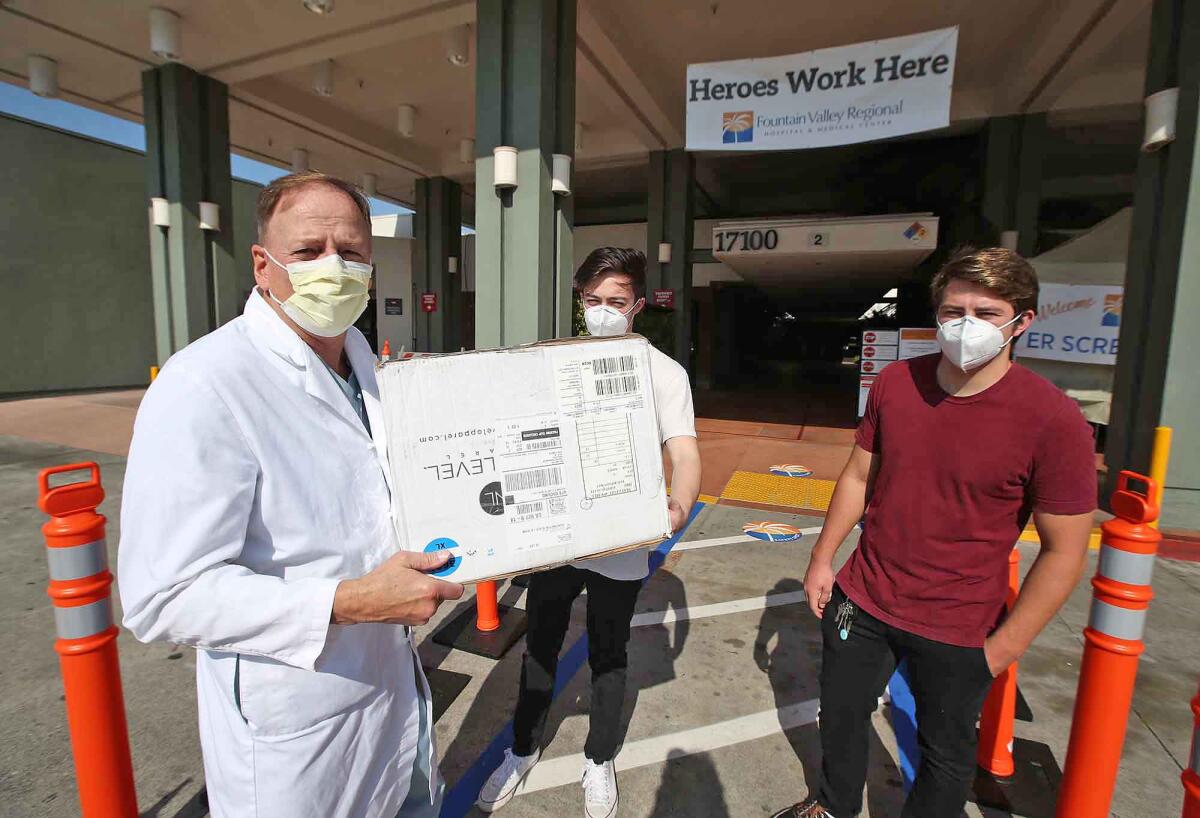 Dr. Tim Korber, left, medical director of emergency services, accepts a box of the first protective masks from Nolen Putnam and Sawyer Farmer to the Fountain Valley Regional Hospital on Monday.