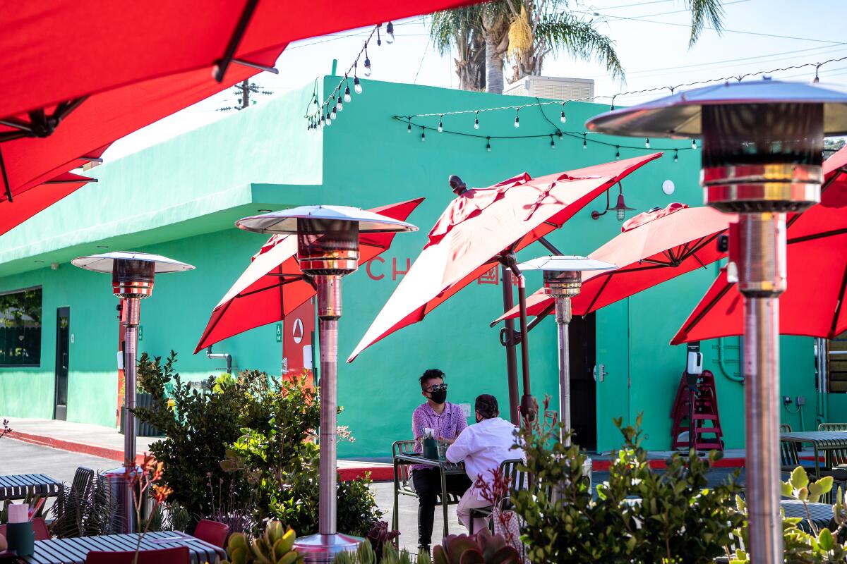 People sit at an outdoor dining area under umbrellas.