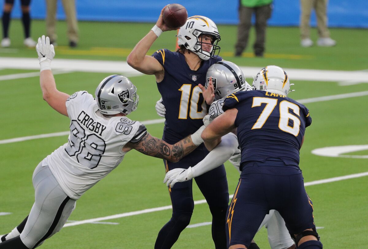 Chargers quarterback Justin Herbert tries to pass before he is sacked by the Raiders' Maxx Crosby and Clelin Ferrell.