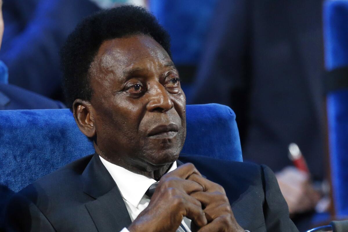 Pele looks to the right while dressed in a suit and sitting in a blue seat.