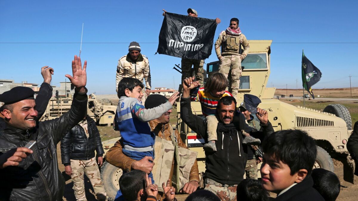 Iraqi army soldiers hold a captured Islamic State flag upside down as they celebrate with residents of Mosul neighborhoods liberated from the militant group on Tuesday.