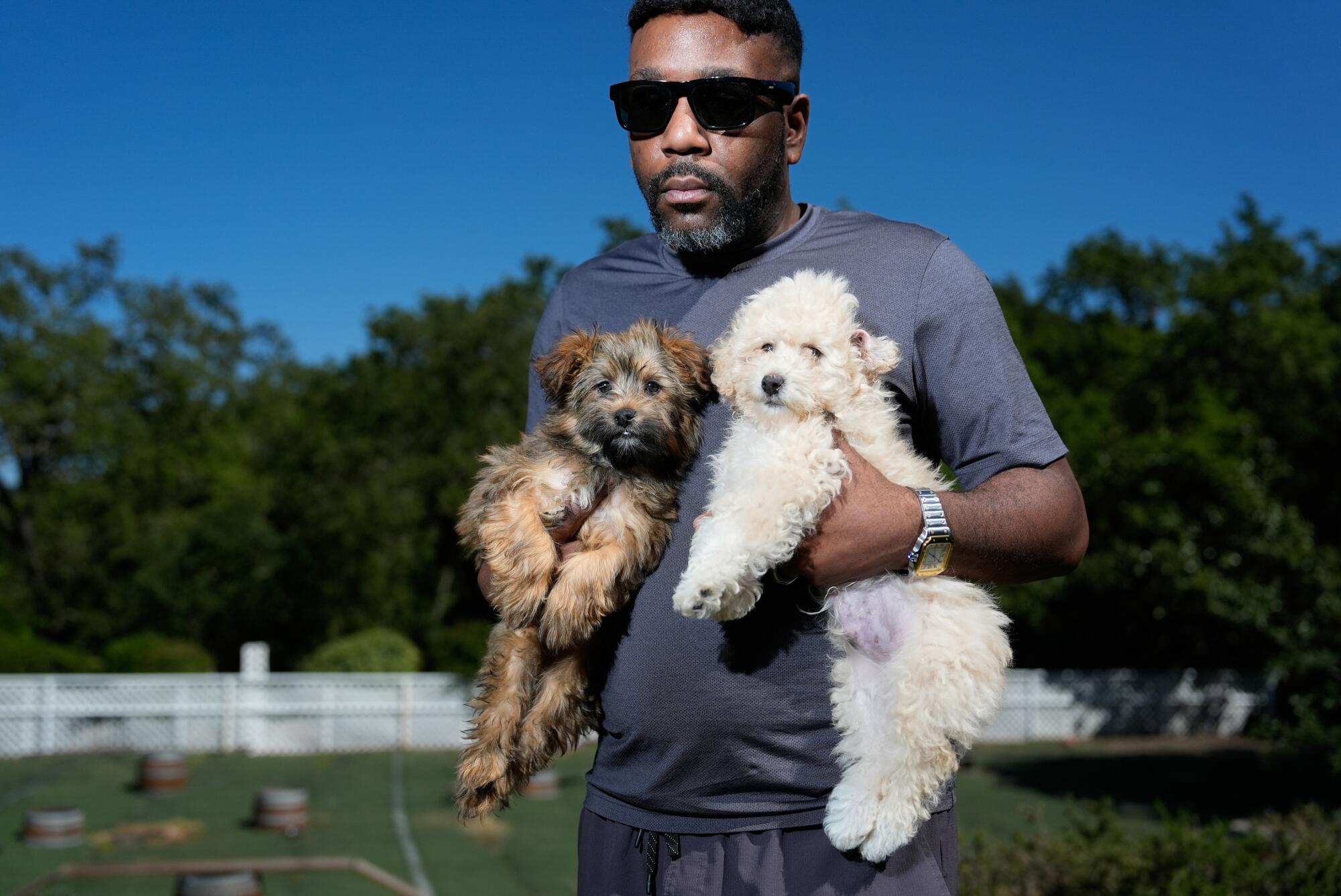 Travis Sneed holding a small dog in each hand at his Los Gatos facility