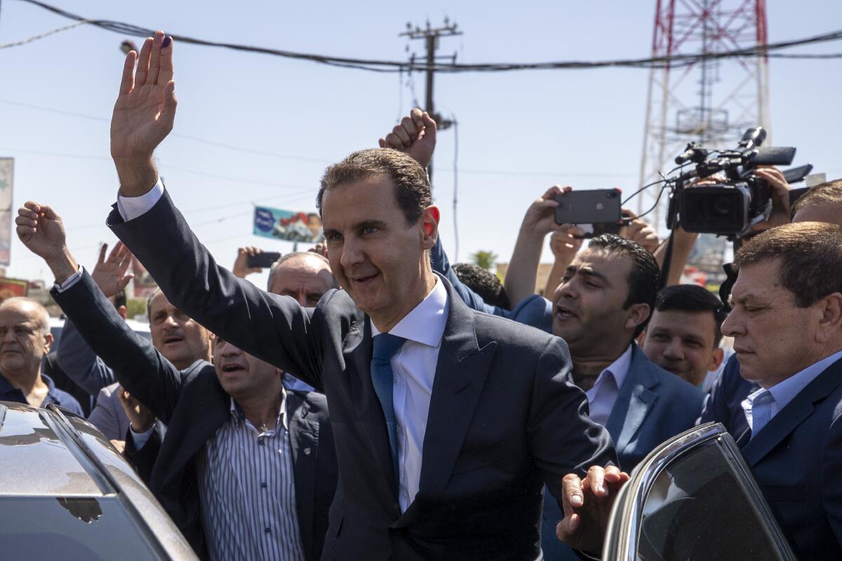 FILE - In this May 26, 2021 file photo, Syrian President Bashar Assad, center, waves to his supporters at a polling station during the Presidential elections in Douma, Syria. Assad issued a decree Sunday, July 11, 2021, giving hundreds of thousands of civil servants and military members a 50% salary increase amid a harsh economic and financial crisis and price increases for vital products. (AP Photo/Hassan Ammar, File)