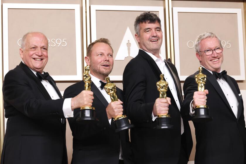 Four men in tuxedos each use one hand to hold their Oscar trophies forward 