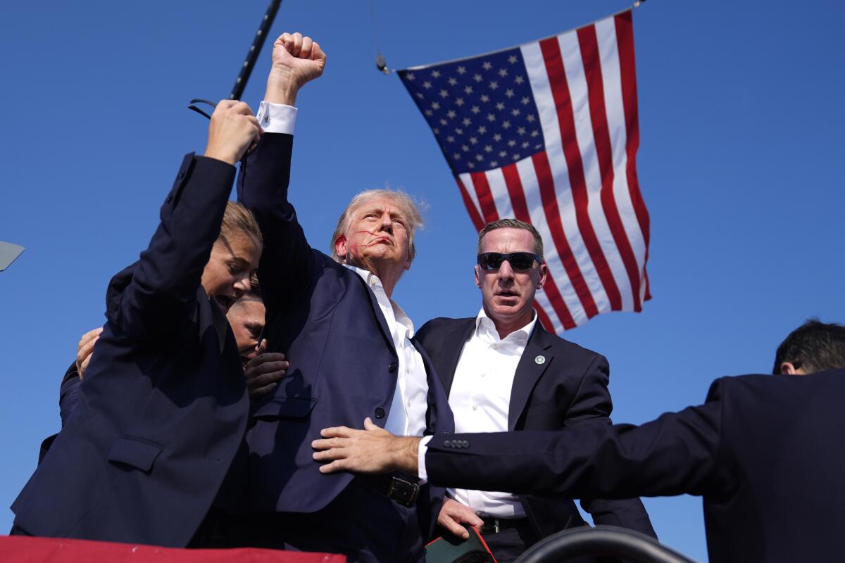 Former President Trump raises his fist as he is surrounded by security agents.