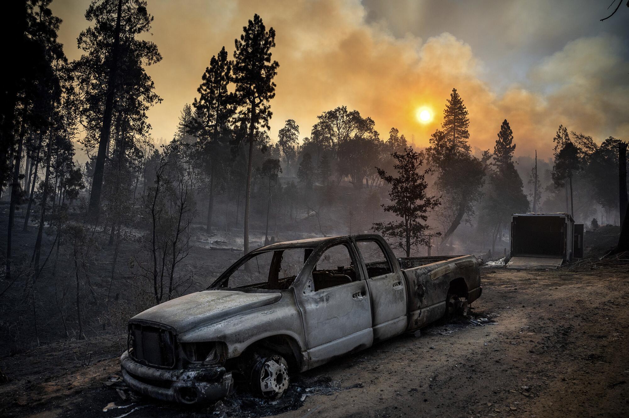 The Oak Fire burns behind a scorched pickup truck in the Jerseydale community of Mariposa County, Calif.