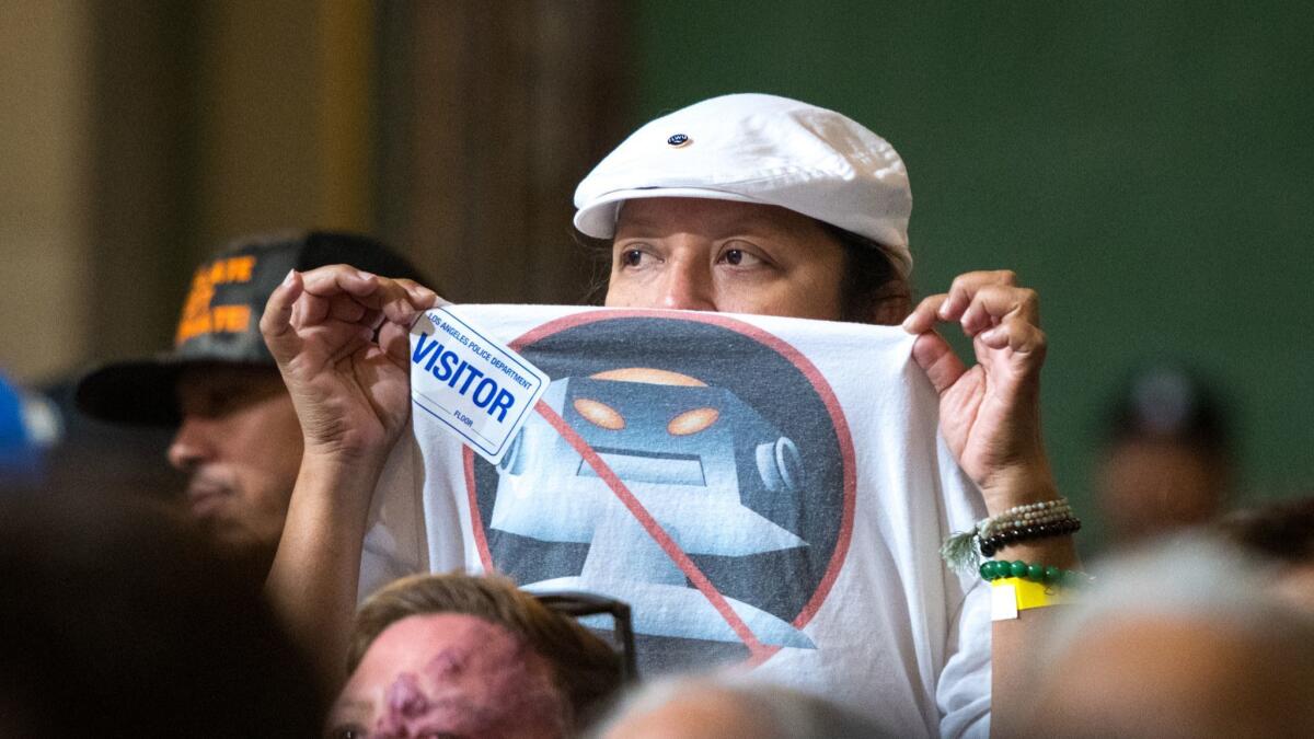 A supporter of dockworkers from the Port of L.A. holds up a "No More Robots" shirt during a Los Angeles City Council meeting on Friday. Hundreds showed up to urge the council to block a plan to allow driverless electric cargo handlers at the port.