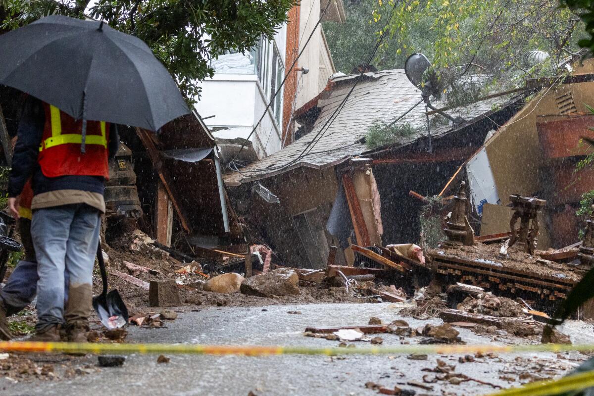 A worker with an umbrella inspects a damaged home.
