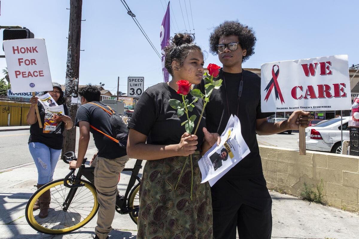 Vishwa Chitnis and Aaron Sanford pass out fliers during a peace "stand-in" at the corner of Maple Avenue and Adams Boulevard in Los Angeles, where USC student Victor McElhaney was shot two months ago.
