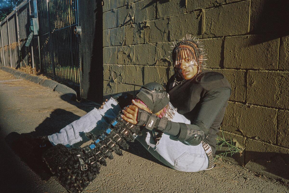 A man with nails in his hair sits against a brick wall
