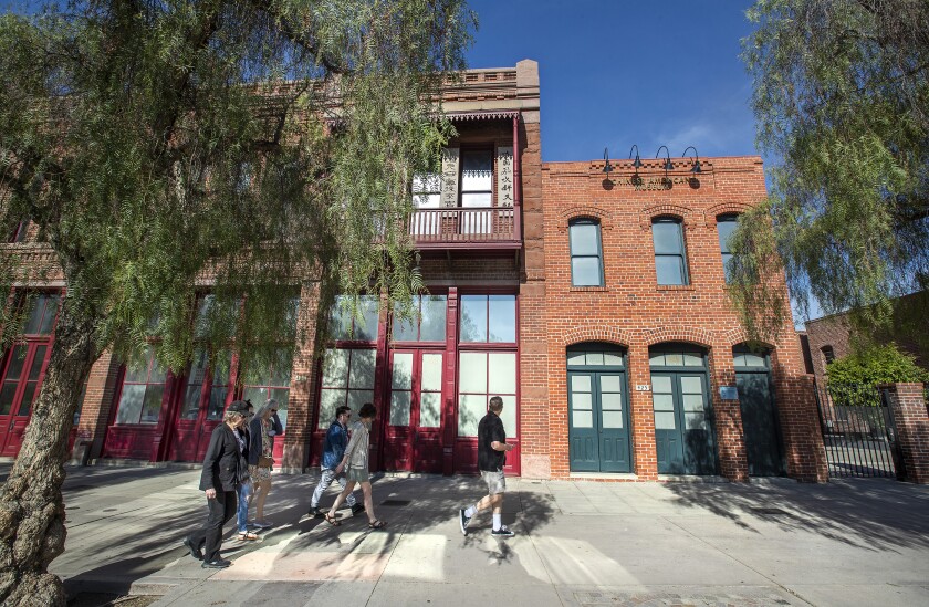 Pedestrians walk along a broad sidewalk in front of vintage brick buildings