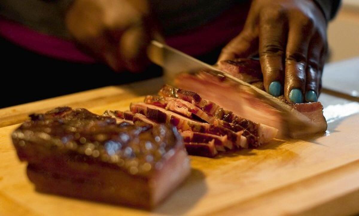 Rashida Purifoy, owner of Cast Iron Gourmet, slices bacon that she cured for seven days and then smoked for three hours over avocado wood.