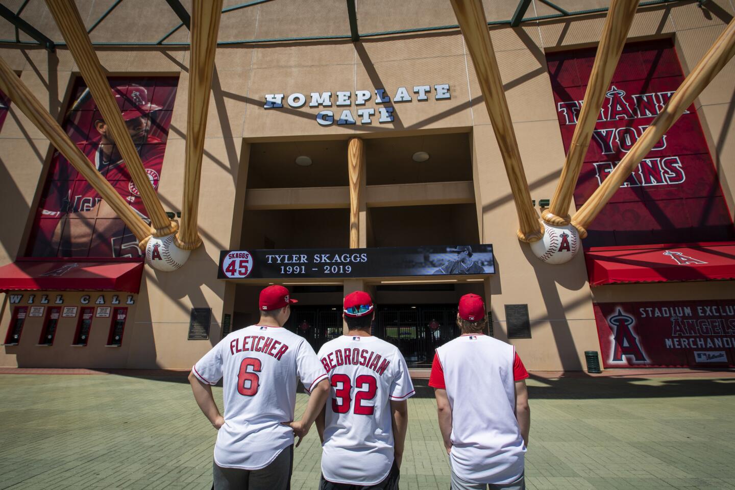 Angels fans Reza Agahi, 18, left, William St. Marseille, 18, center, and Grant Gaynor, 18, all of Anaheim, spend a quiet moment looking at a sign and growing memorial for Tyler Skaggs at Angel Stadium.