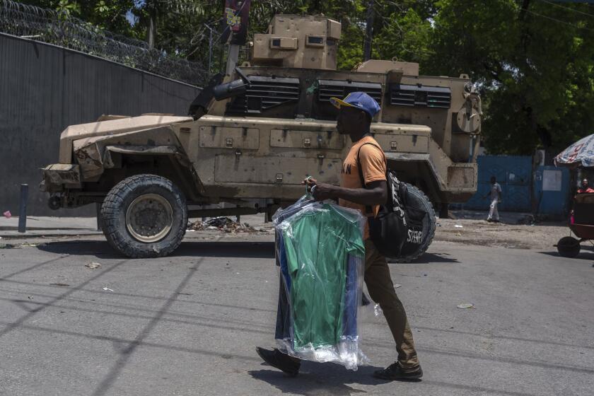 a man carries dry cleaning past an armored police vehicle in Port-au-Prince, Haiti, Sunday, April 28, 2024. (AP Photo/Ramon Espinosa)