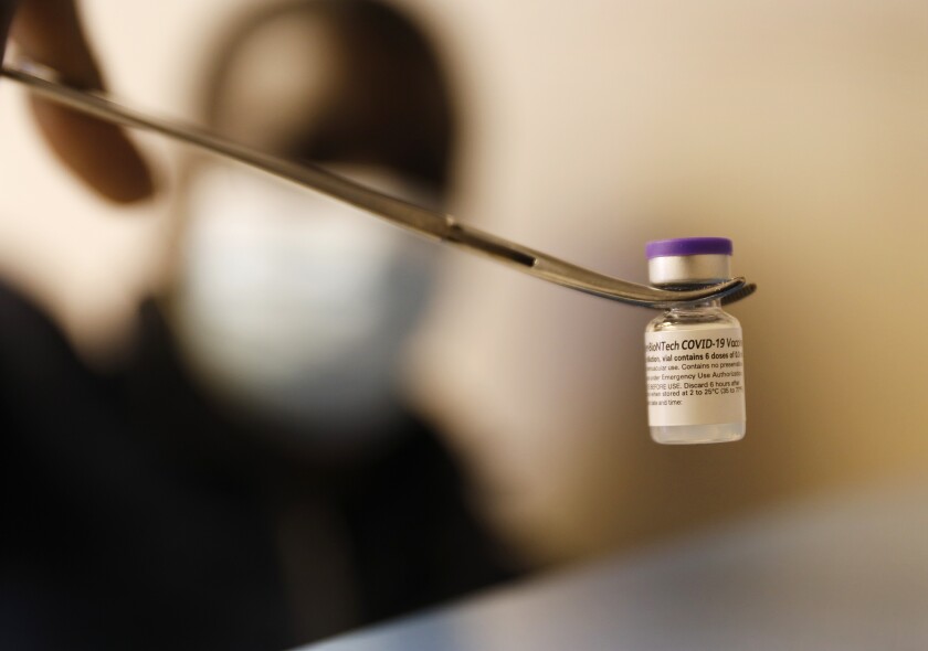 A vial of the Pfizer COVID-19 vaccine is held using a pair of forceps