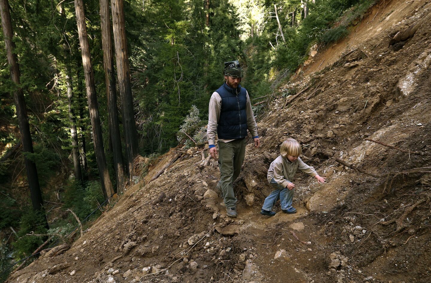 With the road taken out by a massive landslide, Big Sur resident Scott Moffat and his son Roman, 4, hike through muck and debris above the Ventana Inn to get to their truck.