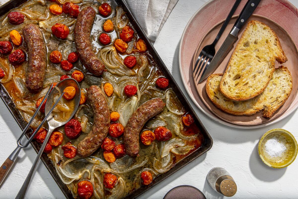 A sheet pan with sausages, onions and cherry tomatoes next to a plate holding toast