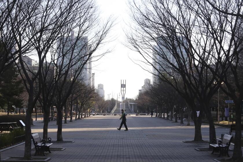 A man wearing a face masks walks along on a nearly empty park in Goyang, South Korea, Sunday, March 22, 2020. For most people, the new coronavirus causes only mild or moderate symptoms, such as fever and cough. For some, especially older adults and people with existing health problems, it can cause more severe illness, including pneumonia. (AP Photo/Ahn Young-joon)