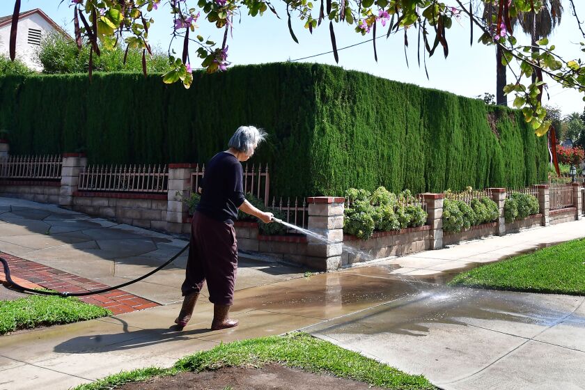 A woman waters down her driveway in Monterey Park