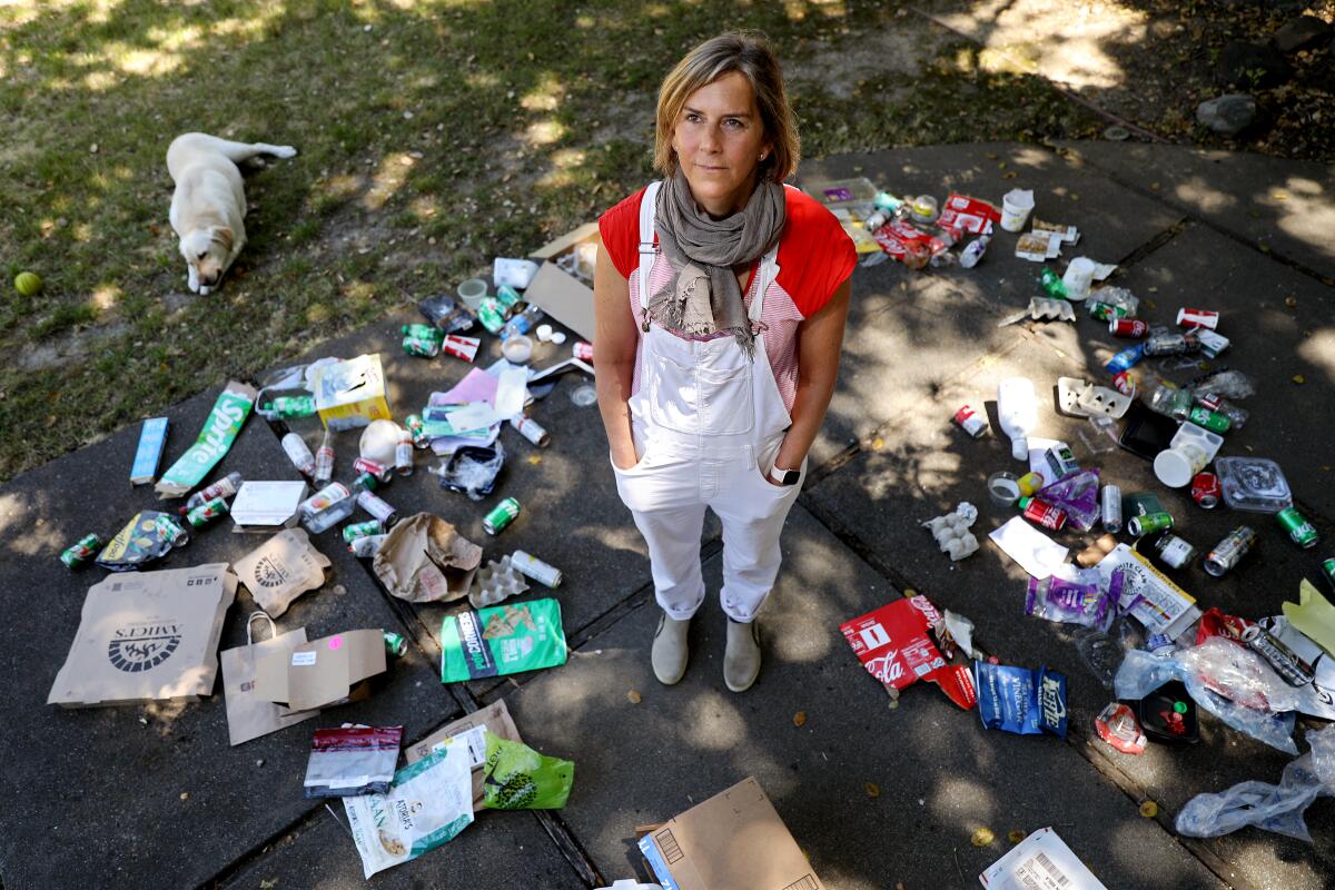 Susanne Rust wearing white overalls standing in the middle of trash scattered on the floor outside her home.
