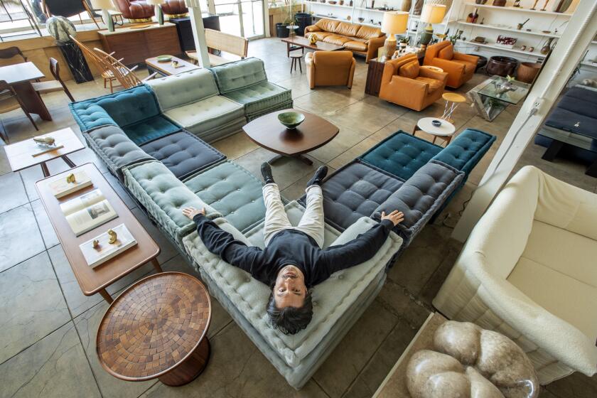 HOLLYWOOD, CA-MAY 8, 2023: Jason Potter, owner of Den, a store specializing in the sale and restoration of 20th century furniture and design, is photographed on a mahjong sofa produced by Roche Bobois. The material is a mix of velvets, boucle and mohair. (Mel Melcon / Los Angeles Times)