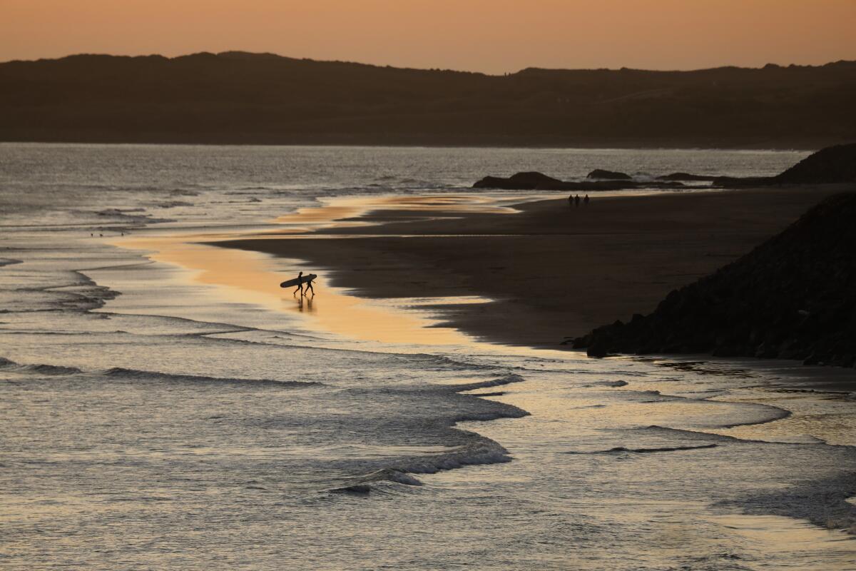 Two surfers walk along Crescent City's coastline at dusk