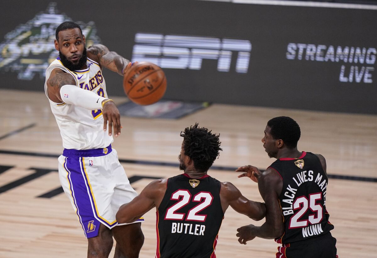 Lakers forward LeBron James flips a pass over Heat defenders Jimmy Butler and Kendrick Nunn during Game 3.