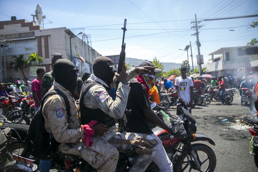 Armed and masked police officers move forward on a motorcycle during a protest by a disgruntled sector of the Haitian police force known as Fantom 509, in Port-au-Prince, Haiti, Wednesday, March 17, 2021. The protests started when officers and police academy cadets marched toward police headquarters to demand that the bodies of five officers killed during a raid last week on the Village of God shantytown be recovered from the gang still holding them. Then things escalated when Fantom 509 stormed several police stations in Port-au-Prince, freeing jailed comrades accused of participating in an alleged coup against embattled President Jovenel Moise. (AP Photo/Dieu Nalio Chery)