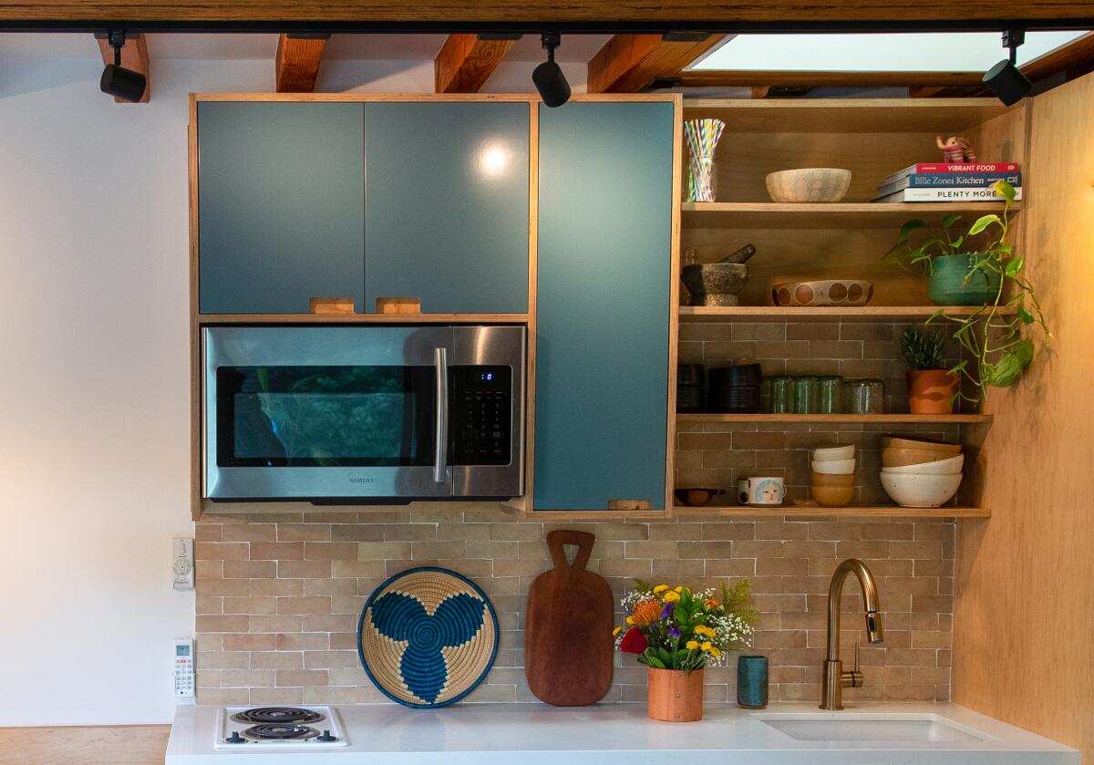 A brown-tiled backsplash below teal cabinets with an orange rim and open shelving filled with cups and bowls.