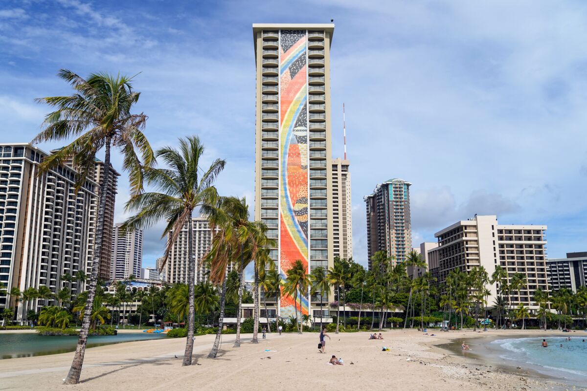 A hotel tower rises over a beach with palm trees