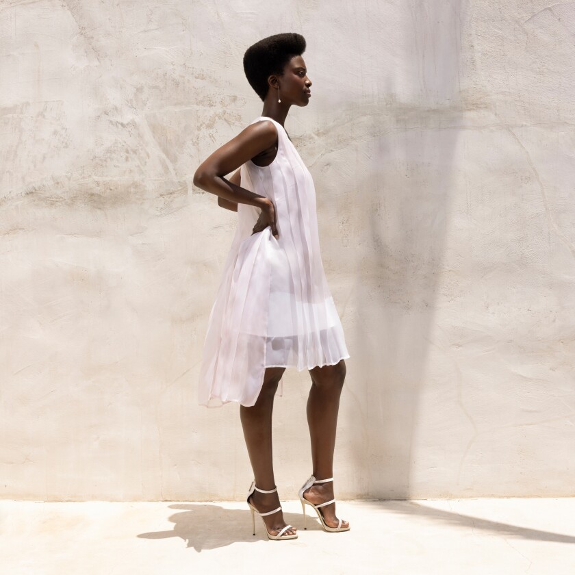 A woman poses in profile in a modern, knee-length take on a post-wedding or bridesmaid's dress.