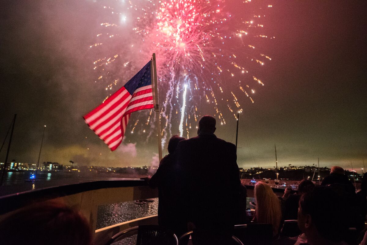 Spectators watch fireworks from a boat, next to an American flag. 