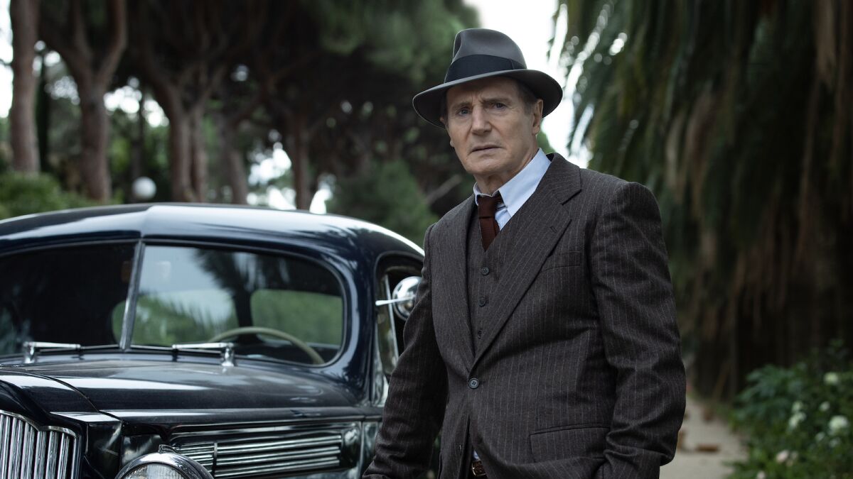 Liam Neeson dans un costume trois pièces et un feutre des années 1940.