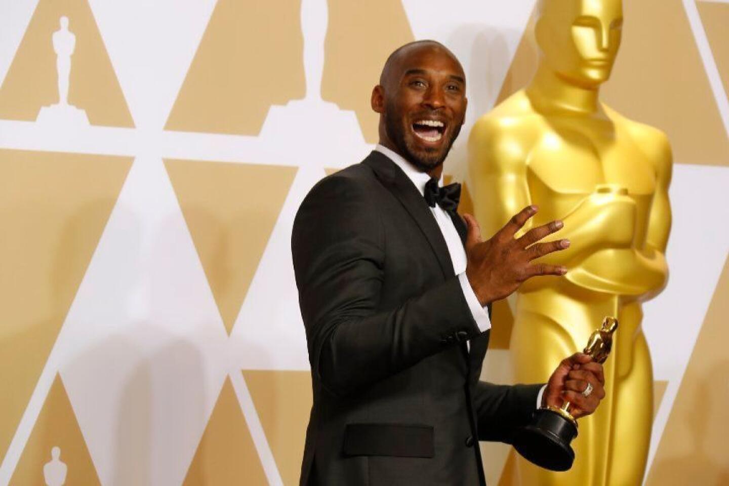 Kobe Bryant, in a tuxedo, holds his Oscar in front of an Oscar statue after winning for "Dear Basketball."