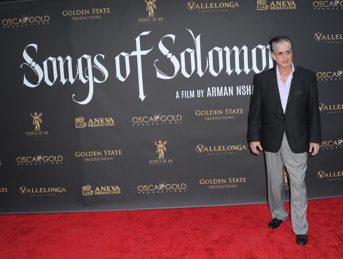 A man in a black blazer stands on a red carpet in front of a backdrop that reads "Songs of Solomon."