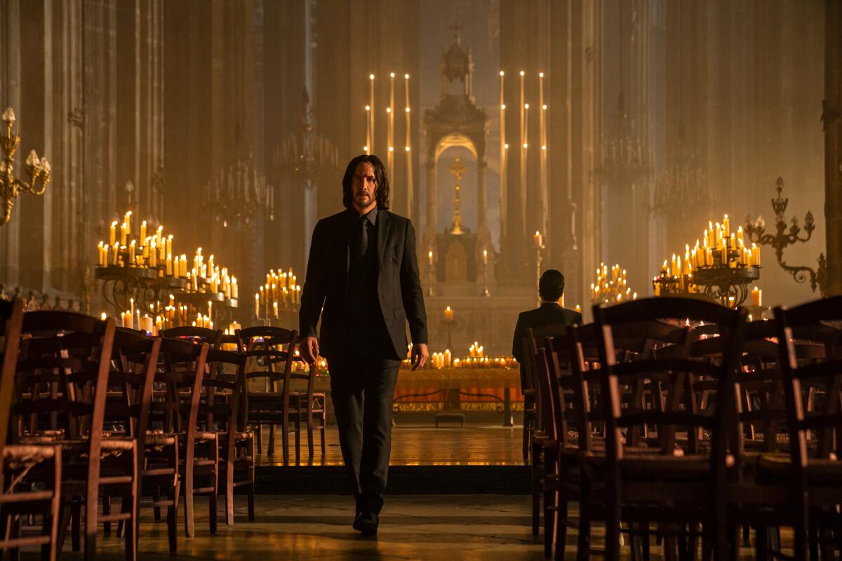 John Wick walks through a church filled with candles and rows of chairs.
