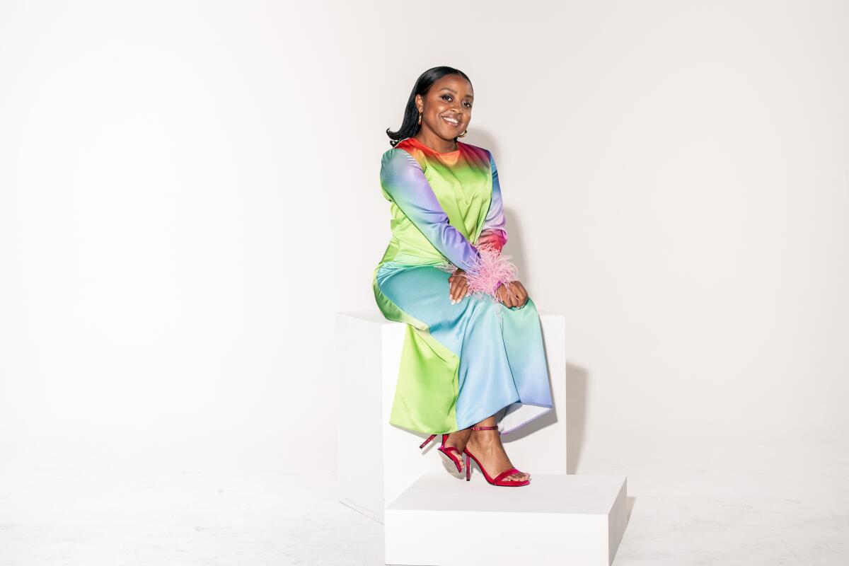 Quinta Brunson sits on giant blocks wearing a long colorful dress for a portrait.