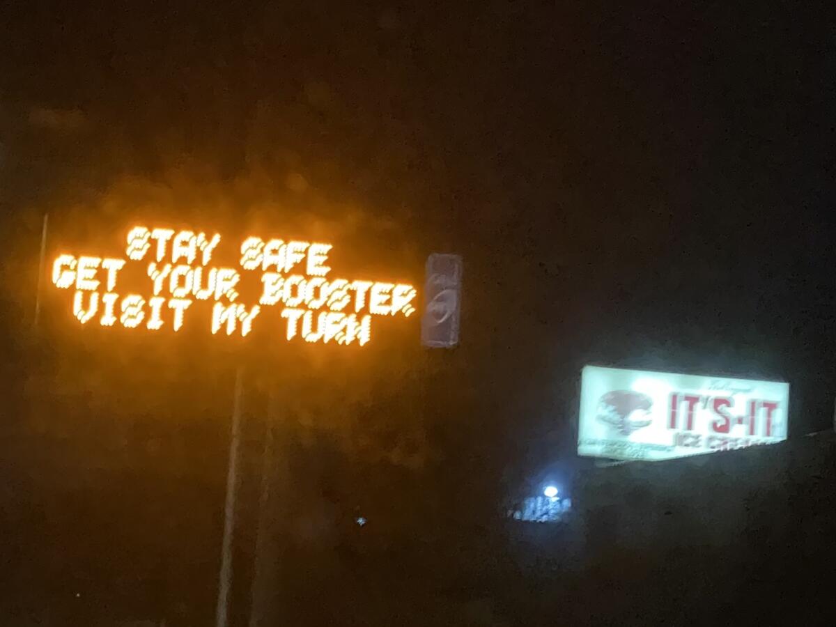 An electronic freeway sign says "Stay safe, get your booster, visit My Turn."