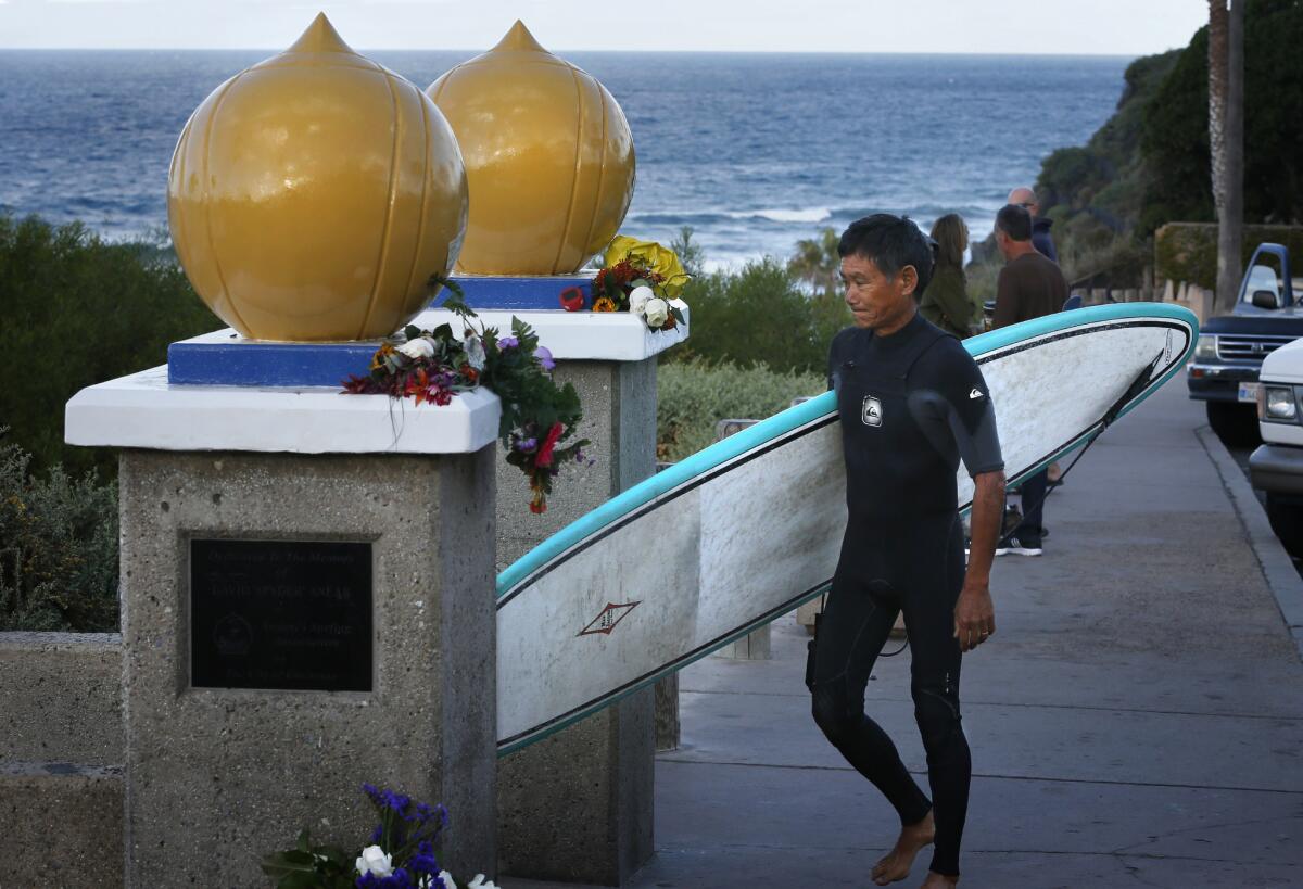 Local surfer Calvin Tom frowns as he walks past flower memorials to two surfers who died recently at Swami's Beach in Encinitas.